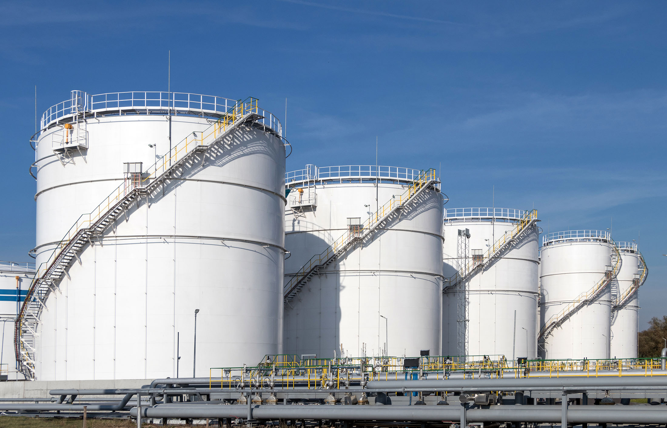 A row of tanks on a tank farm with blue sky in the background.